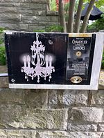 Box showing assembled chandelier with floral and crystal accents on black background.