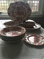 Tilting view of stacked dinnerware showing bowls, plates and serving tray with English Chippendale red floral pattern