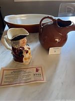 Photo showing the hand painted Wood Potters of Burslem Toby Jug, brown Hall pitcher, long ceramic casserole dish, and certificate of authenticity