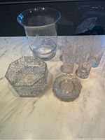 Full view of the crystal serving bowl, etched glass vase, small serving plates, and six glasses on marble counter