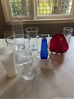 Wide view of all nine assorted vases varying in shapes, colors including white milk glass, blue, red, clear glass, and crystal. Shows overall assortment and size differences.