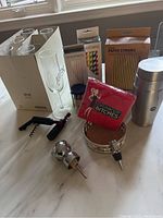 Photo showing six champagne glasses in original box, red napkins, paper straws, cocktail shaker, corkscrew, wine stoppers, and a cork-lined wine holder on a white countertop.
