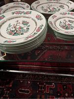 Stack of plates showing floral and tree motif with pink, green, and brown colors and gold Greek key border