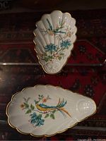 Top view of first Limoges porcelain trinket dish showing scalloped edges, gold trim, and colorful bird with floral design on white background.