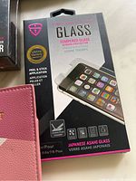 Photo of iPhone tempered glass screen protector packaging and partial view of pink passport case