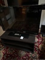 Sharp large screen TV on the dark wood stand showing front view with remote placed on the stand.