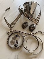 Lot of mixed sterling silver and silver-tone metal jewelry including bracelets, earrings, necklaces, and charms on a light surface.