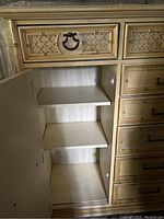 Inside view of the side cabinet showing two internal wooden shelves and door with metal ring pull.