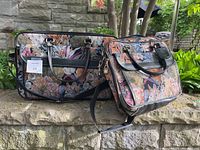 Both pieces of the vintage floral tapestry luggage set displayed outdoors with greenery background