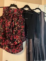 Three women's clothing items hanging on black and white hangers: a floral sleeveless blouse, a black cardigan, and a striped sleeveless maxi dress.