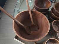 Large wooden salad bowl with two wooden serving utensils inside showing the natural wood grain finish.