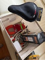 Photo of basket interior showing black ZIPLO Extra Gel bike seat, orange extension power cord, white smart light bulb and cables, and portable lantern in a box.