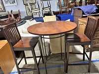 Full view of round wooden bistro table with two matching wooden chairs in a warehouse setting, showing used condition.