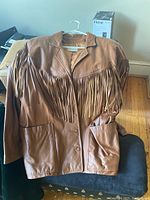 Brown leather jacket with long fringe across the chest and large front pockets on a hanger.