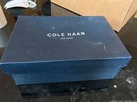 Closed blue Cole Haan branded shoebox on a black surface.