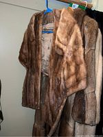Brown fur coats hanging on a rack showing various textures and colors.
