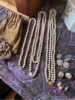 Photo showing all pearl necklaces laid out on patterned fabric alongside four pairs of earrings and two brown velvet pouches.