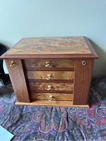 Closed wooden jewelry box showing natural wood grain pattern with four drawers and brass knobs, side keyhole and lock