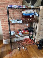 Black metal wire rack shelving unit against brick wall, showing items on shelves but sale excludes contents.