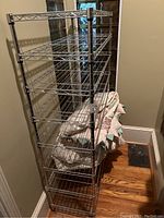 Full view of the five-tier metal wire storage shelf with folded quilts on one shelf, shown on hardwood floor in a narrow space.