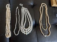 Five pearl necklaces lying on a black surface showing variety in styles and pearl sizes