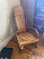 Wooden rustic-style rocking chair with branch-like supports and high slatted backrest against a wall