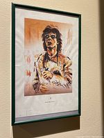 Framed screen print showing a stylized portrait of a musician in a green frame hung on a beige wall.