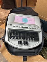 Clink Cybra electronic stenograph machine with digital display and plastic keys, sitting in black soft carrying case.
