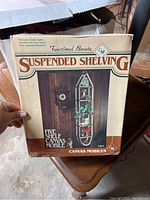 Box showing product packaging and name 'Suspended Shelving' by GM with image of shelving unit filled with decorative items.