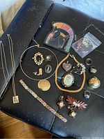 Overview of assorted western-themed jewelry displayed on black surface showing chains, pins, rings, and earrings.