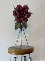 Close-up of artificial dark red flower with leaves, attached to wooden ring holding the chime tubes.