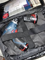 Cordless drill with two batteries secured in black fabric carrying bag