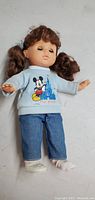 Front view of the 13-inch vintage doll wearing a light blue sweatshirt featuring Mickey Mouse and Blue Castle print, denim jeans, and white shoes. The doll has brown hair in two pigtails.