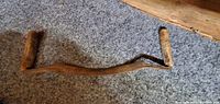 16-inch antique shaving tool laid on carpet showing wooden handles and rusty metal bar with uneven bends.