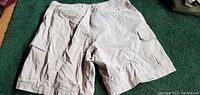 Front view of the beige men's cargo shorts showing two large thigh pockets with flaps and a button closure.