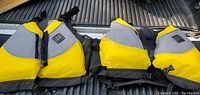 Two yellow and gray adult life jackets with black straps placed side by side on a truck bed surface.