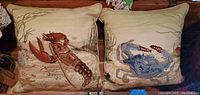 Pair of needlepoint pillows showing lobster on the left and crab on the right with beige underwater themed background.