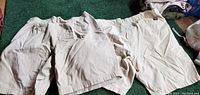 Two pairs of men's cargo shorts laid side by side on green carpet. Both in beige tones, showing front and pockets.