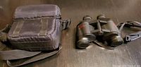 Binoculars and carrying case placed on dark surface showing overall condition.