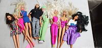 Photo showing 8 vintage Barbie dolls laid out on a flat surface, 7 female and 1 male doll, different colored outfits and hairstyles.