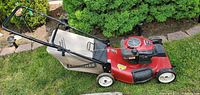 Side view of Craftsman lawn mower showing red metal deck, black engine cover, pull cord, and Dust-Blocker grass bag attached to handle.
