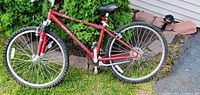 Red Schwinn girls front suspension mountain bicycle leaning against a garden wall. Visible details include frame structure, tires, seat, handlebars, and pedals.