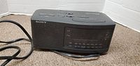 Front and left side view of the black Sony Dream Machine clock radio showing speaker and AM/FM radio dial.