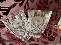 Two transparent glass lampshades with white floral etching placed on patterned fabric background