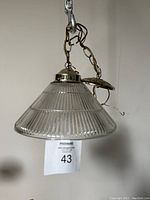 Full view of the hanging light with ribbed clear glass conical shade and metal hardware chain