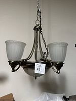 Front view of brass ceiling light fixture with three frosted glass shades and chain for mounting