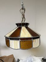 Side view of vintage stained glass hanging light fixture showing amber and cream glass panels with metal framing and chain suspension.