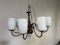 Front view of chandelier showing six white ribbed glass shades and bronze-toned metal curved arms.
