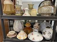 Wide view of multiple antique glass shades and decorative glass pieces on a metal shelf.