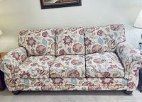 Front view of a three-seat sofa with floral patterned upholstery over an off-white fabric background.